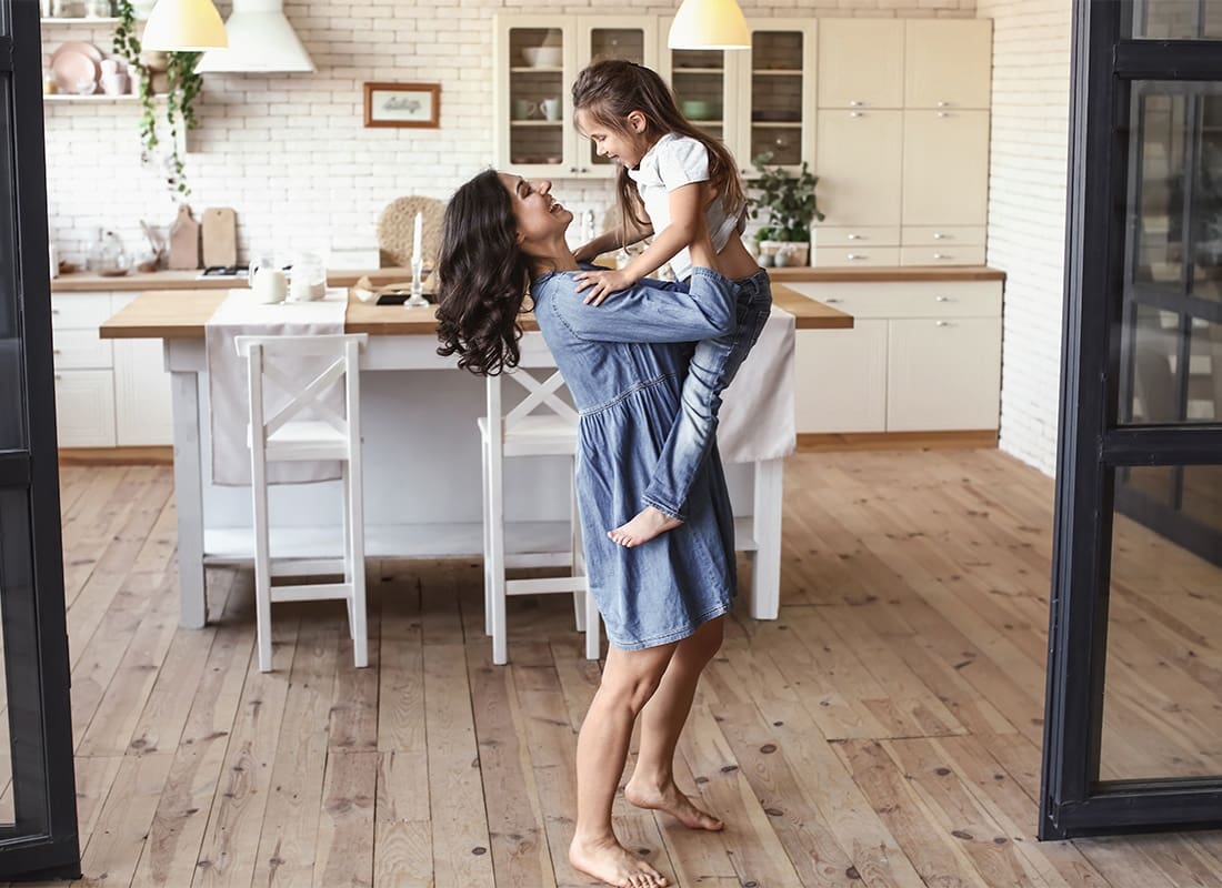 Personal Insurance - Portrait of a Cheerful Mother Holding Up her Daughter While Standing in the Kitchen